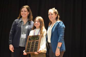 Mary Ann Olsommer and Joann Strattman stand with fifth-grade winner Aria Gonzalez, who correctly spelled “newfangled” for the victory.