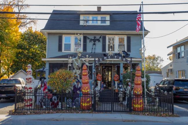 <b>This homemade cemetery display on E Main St. in Port Jervis, NY features a flag pole-climbing skeleton, jack-o’lantern towers, and Chucky doll on the porch to welcome trick-or-treaters. (Photo by Aja Brandt)</b>